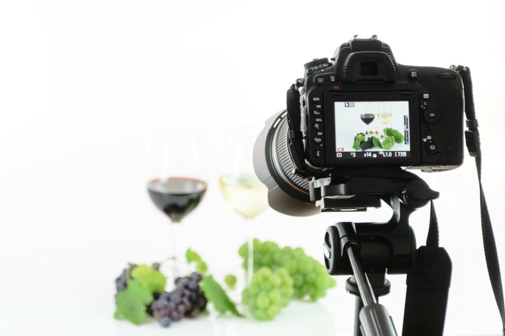 A black full frame DSLR camera captured a photo of purple and green grapes and two wine glasses half-filled with wine in a studio