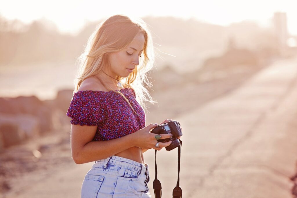A woman wearing a floral crop top is holding a black DSLR camera on an empty road