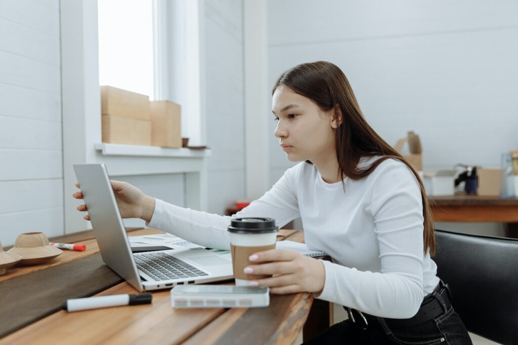 Een vrouw in witte lange mouwen en zwarte broek met een zilveren Macbook op een bruine houten tafel