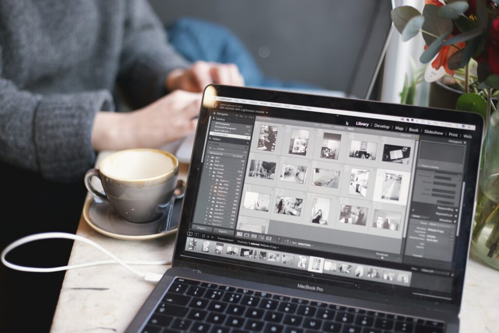 A person wearing a gray sweatshirt is sitting near an empty coffee cup and a black laptop on a white table