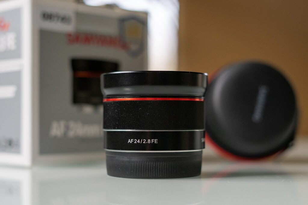 A black 24mm camera lens beside a box placed on top of a white table