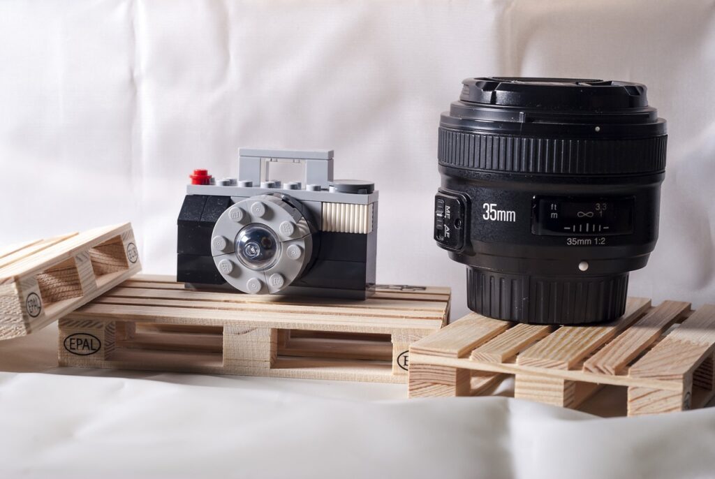 A black 35mm lens beside a camera lego toy placed on a brown wooden pallet board