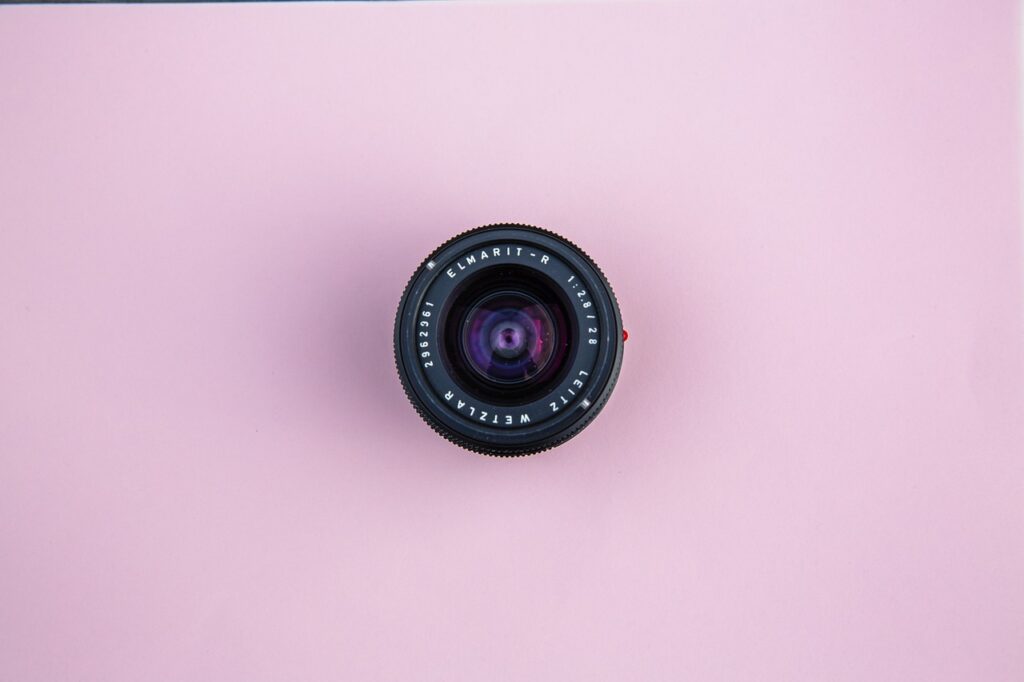 Una vista superior de una lente negra de 28 mm Leitz Wetzlar colocada sobre una superficie rosa