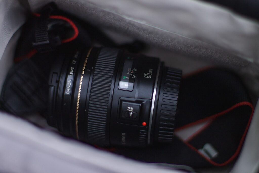 An 85mm Canon lens and a black Canon strap are placed on a camera bag