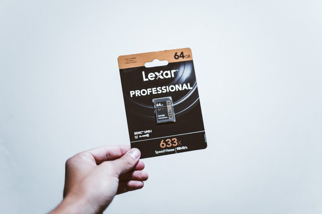 A person holding a black Lexar 64GB SD card pack near a white wall