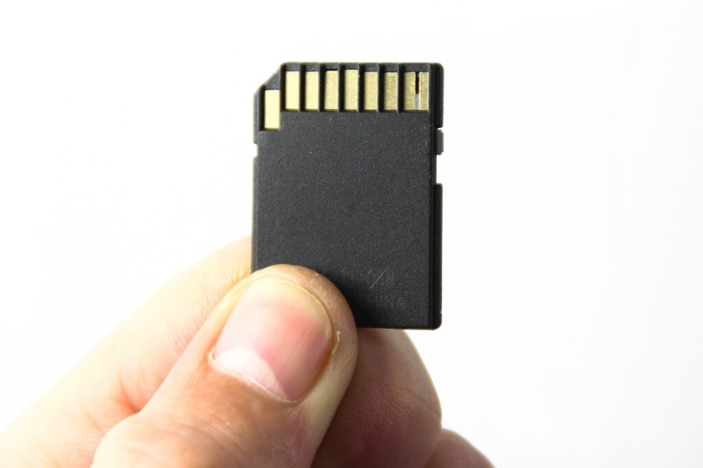 A person with clean nails is holding a black memory card near a white wall