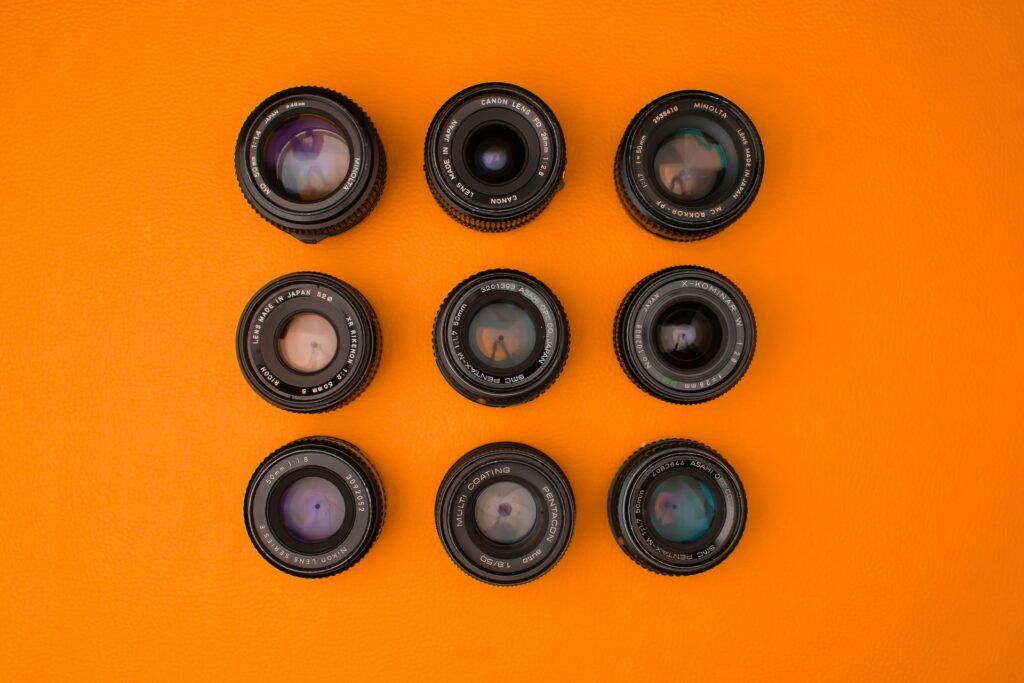 Nine Đen camera lenses lined perfectly on top of an orange surface