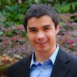 Harry Lim wearing a black suit and blue long sleeves shirt while smiling near fresh plants and flowers