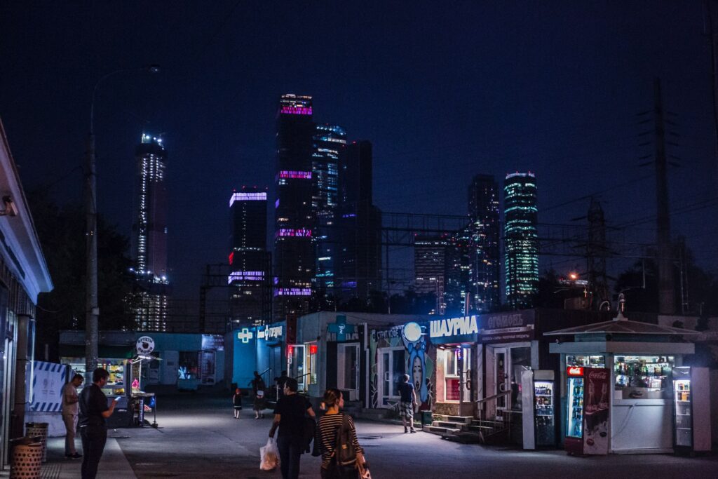 People walking on a road near an open convenience store overlooking the tall buildings