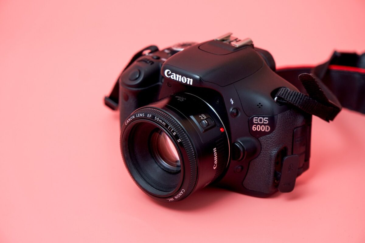 A black Canon DSLR camera with a 50mm lens and black strap placed on a pink surface