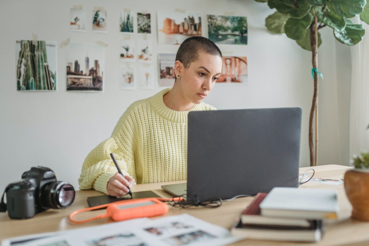 A woman wearing a yellow knitted sweater is using a black laptop placed on top of a brown wooden table