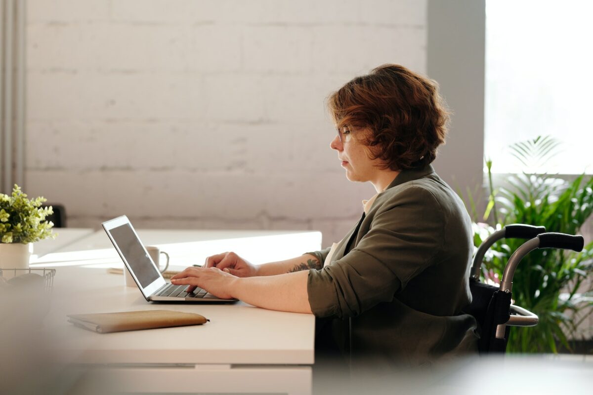 A woman in green long sleeves using a laptop placed on a white table