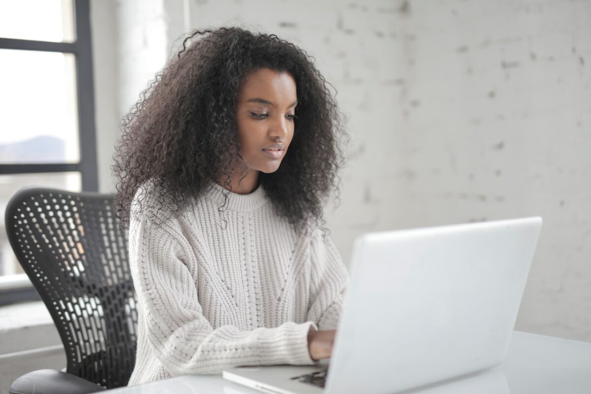 A woman in a white knitted sweatshirt uses a white laptop placed on a white table