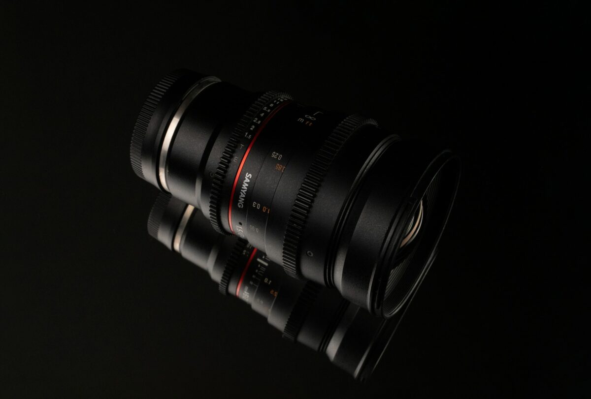 A black 24mm Samyang camera lens placed on a mirrored surface