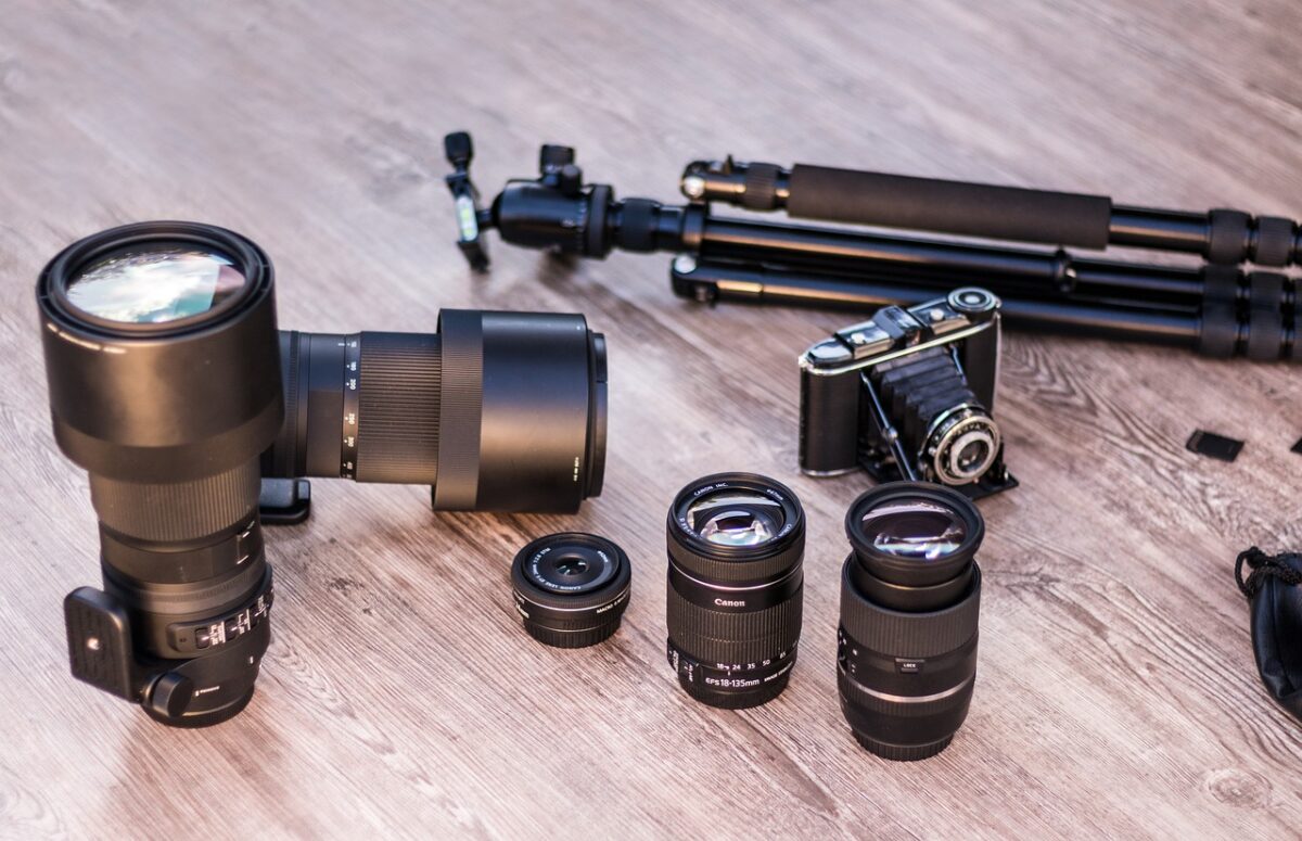 Different camera lenses, an analog camera, and tripod are placed on a wooden surface