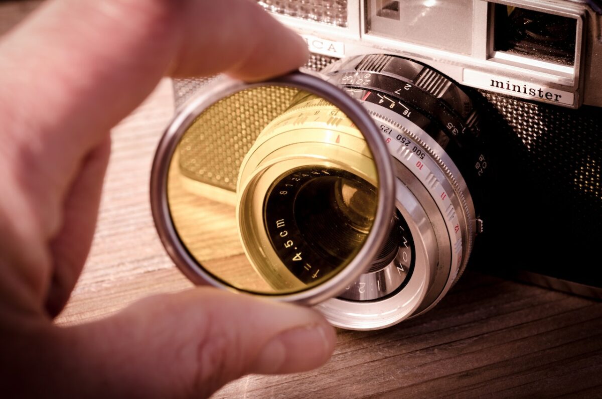 A person holds a camera filter near a camera placed on a wooden surface