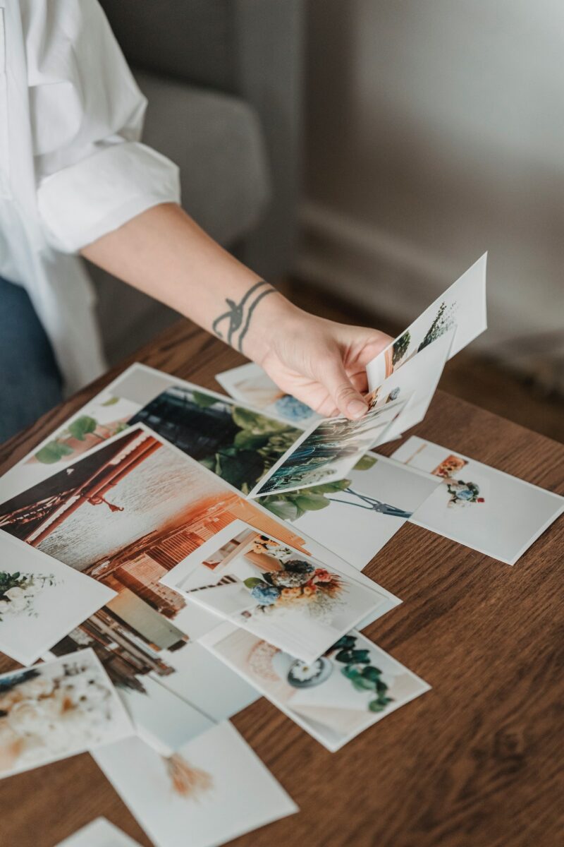 Uma pessoa de manga comprida branca olhando para as fotos impressas colocadas sobre uma mesa de madeira