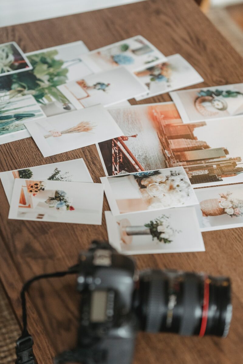 A black DSLR camera with printed photos scattered on a brown wooden table