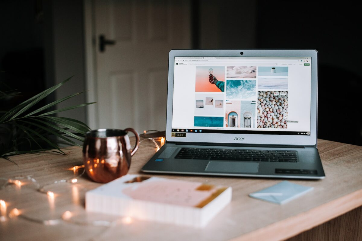 A silver Acer laptop near a rose gold colored mug and book on top of a brown wooden table