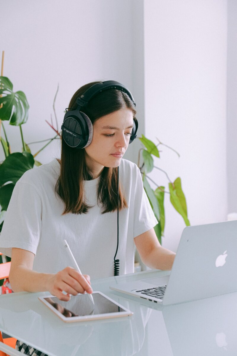 A woman in a white t-shirt using a white tablet and Macbook placed on a white table