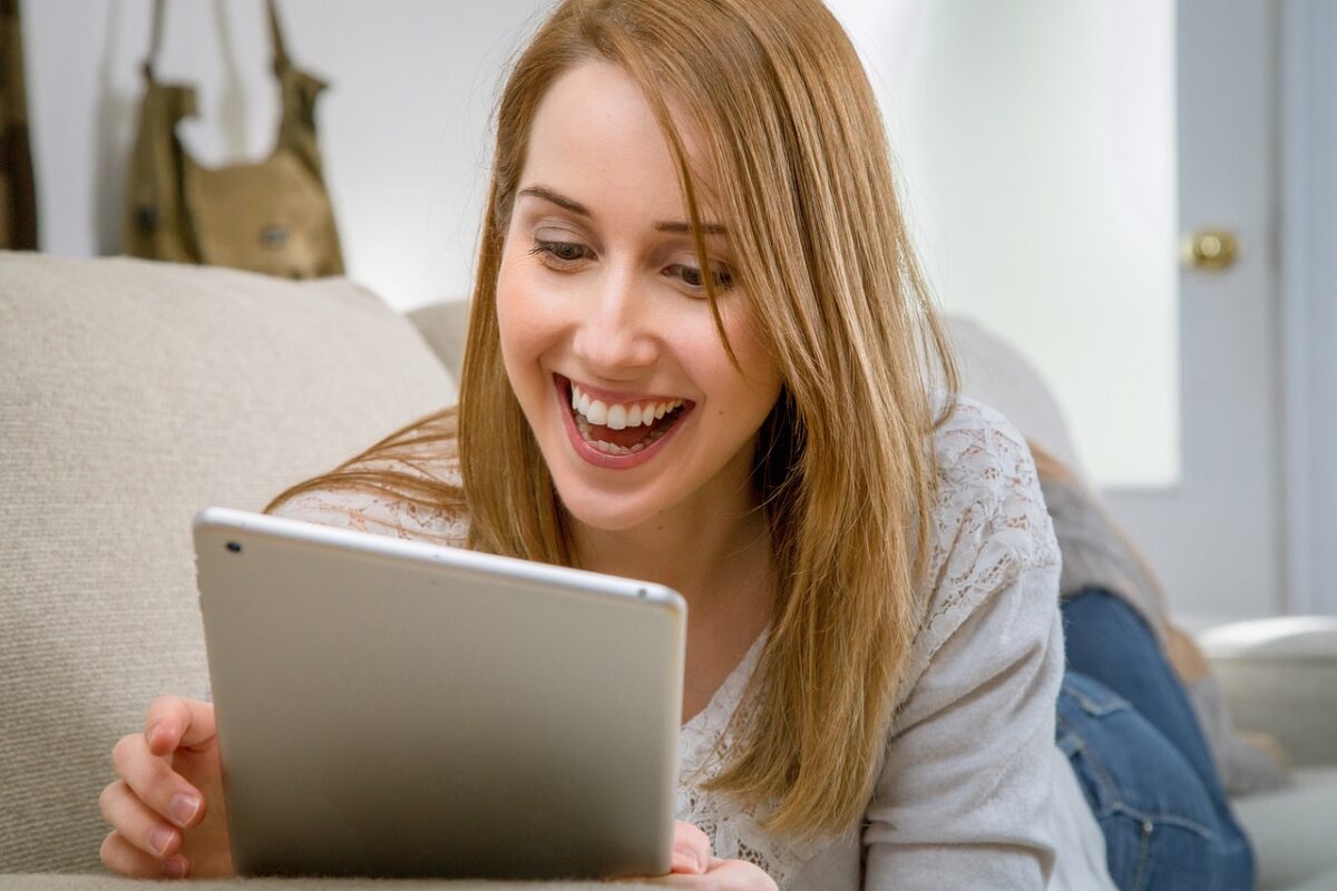 A woman in a white blouse and denim jeans uses a white tablet