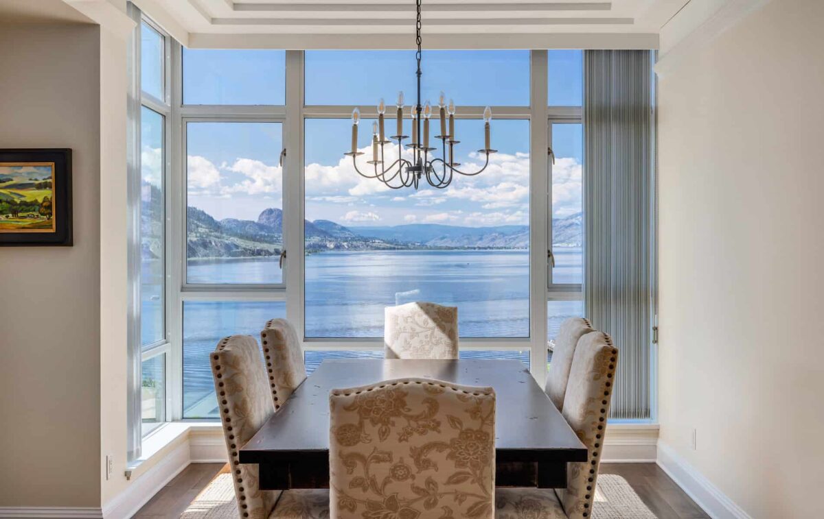 Formal dining room with a dark brown wooden table and upholstered white printed chairs with tall glass windows overlooking the ocean