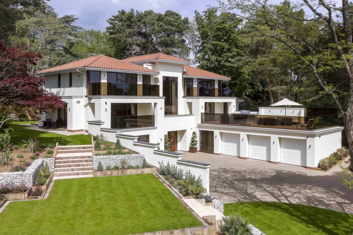 Elevated exterior shot of a three story white mansion with a spacious lawn and driveway