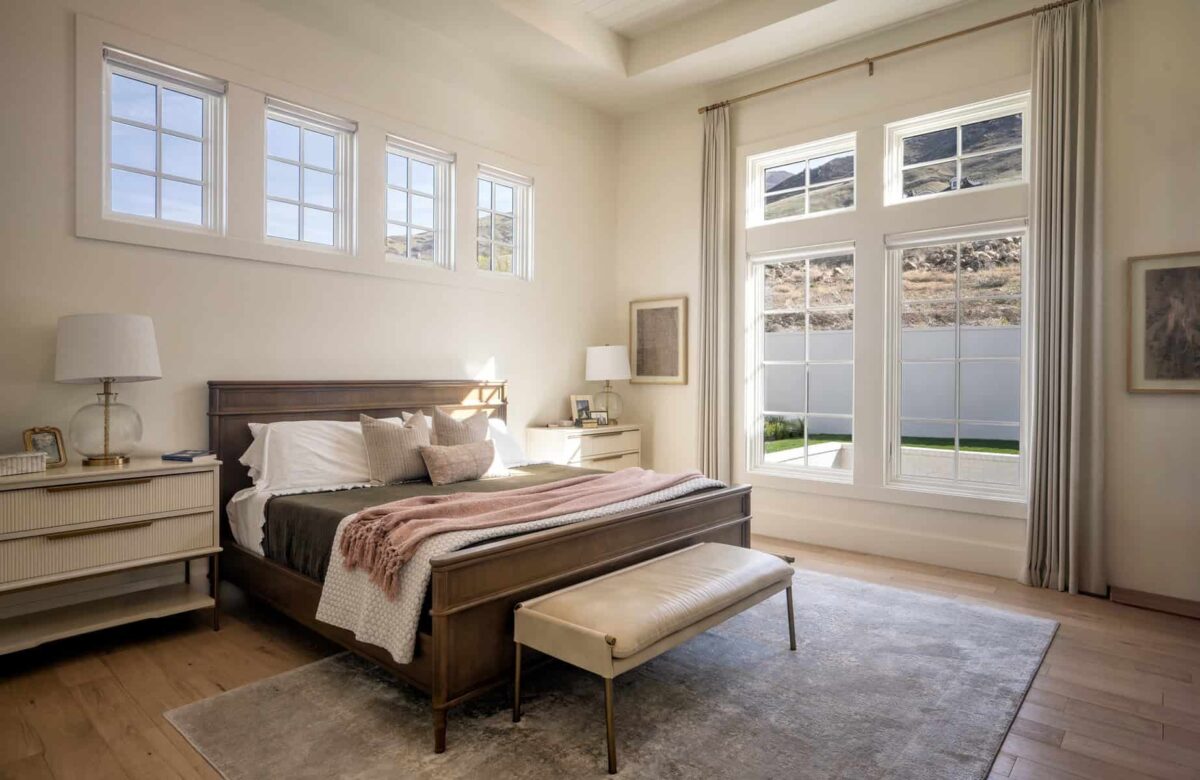 A cozy and modern bedroom with neutral tones, large windows allowing natural light to flood the space, and a plush bed with soft textile