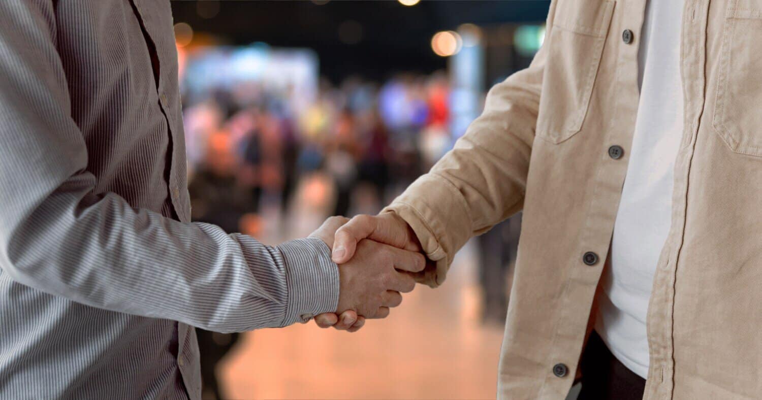 Two people shaking hands in a blurred, professional setting.
