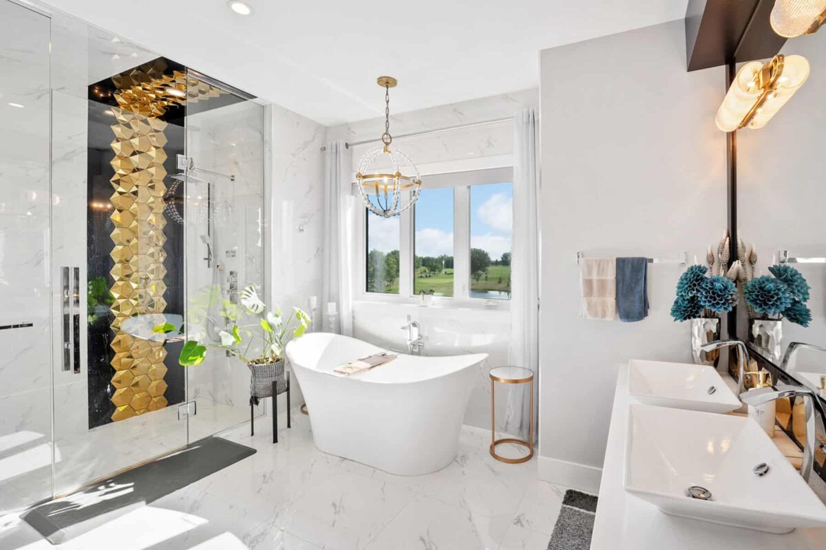 Luxurious modern bathroom featuring a freestanding tub, dual sinks, a glass shower with gold geometric tiles, and a large window with a scenic view.