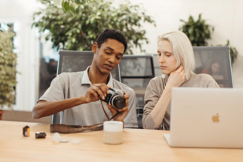 Man showing his camera to a woman working on her laptop