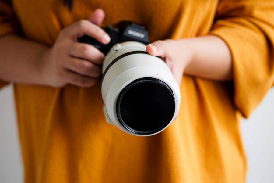 Person in mustard colored shirt holding a Sony camera with lens