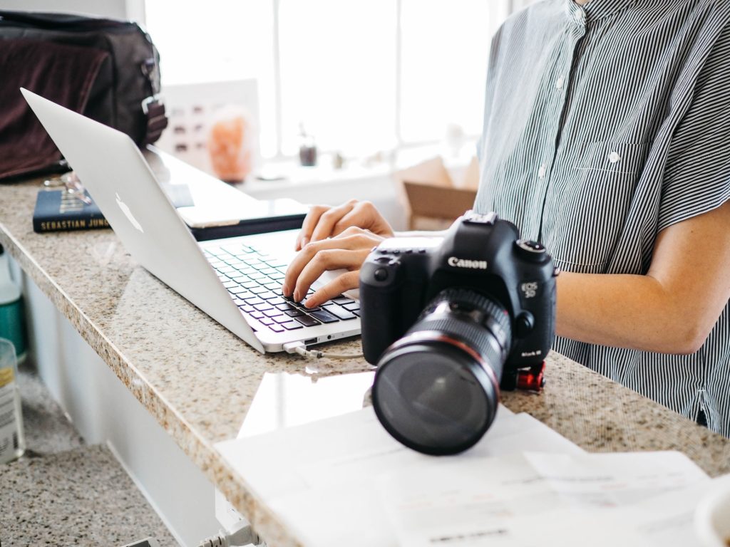 使用 MacBook 使用 Photoshop 进行编辑的人旁边的佳能相机